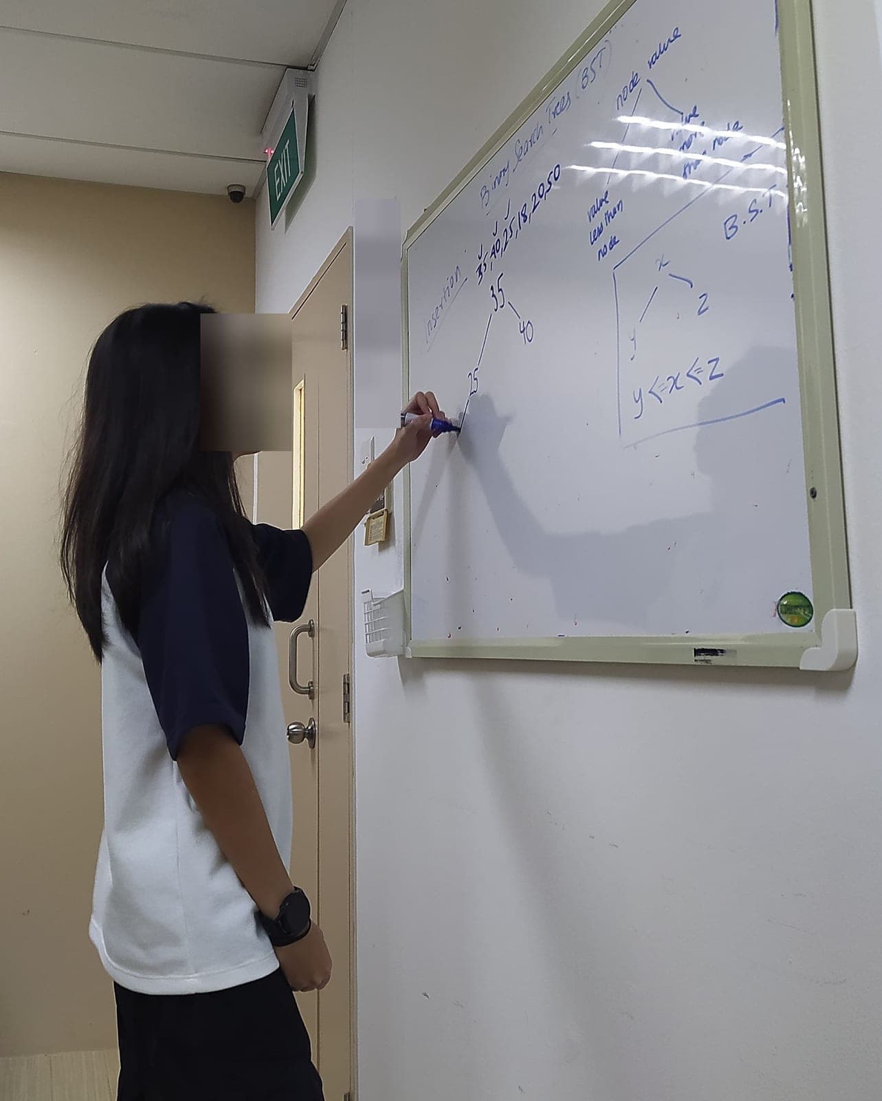 A student drawing a binary search tree on a whiteboard, face blurred
